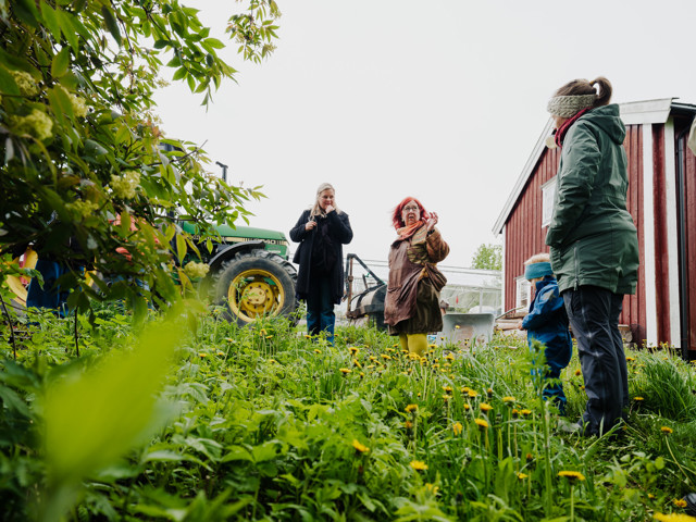 Bilde av flere folk som står i enga på en gård